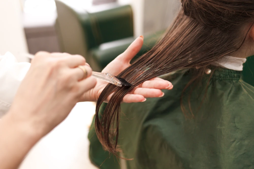 Stylist applying keratin hair treatment on wet hair.