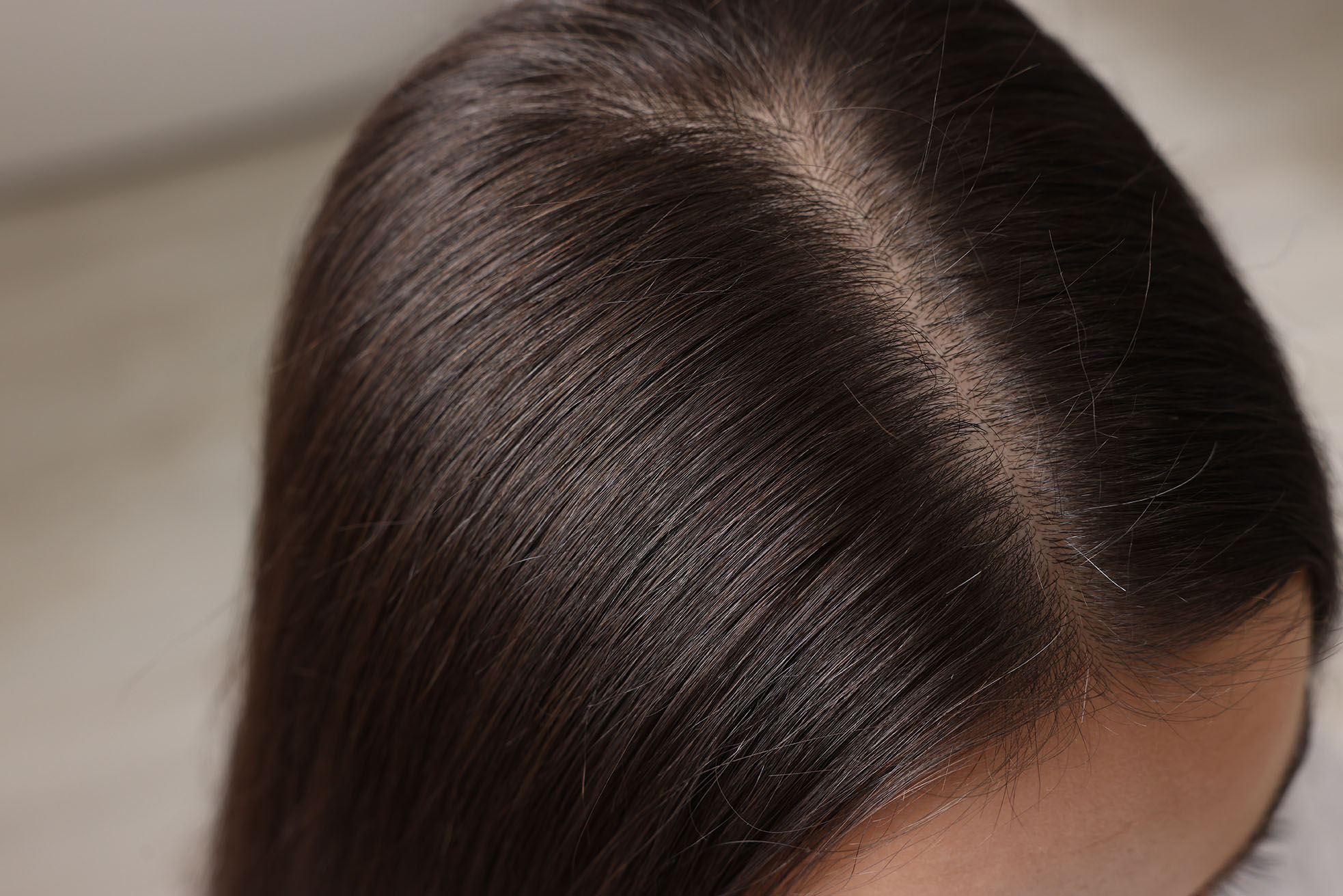 close-up of a person’s clean scalp with smooth brown hair parted down the middle