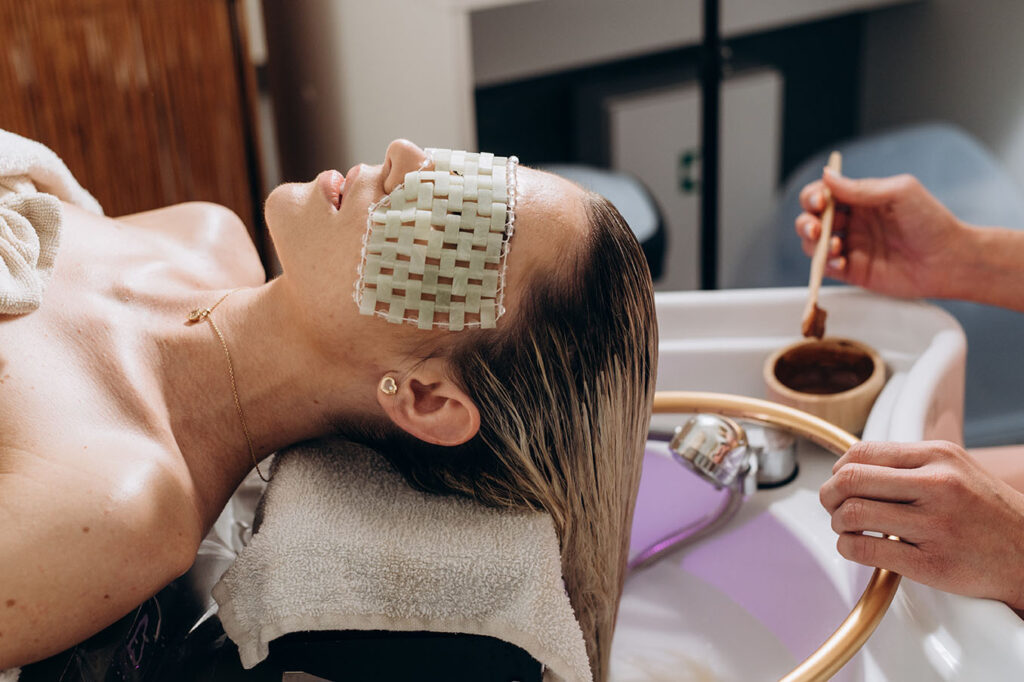 woman with long dark hair gently touching her scalp with both hands