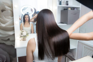 Woman with long, shiny, straight hair looking in the mirror after receiving a keratin hair treatment.