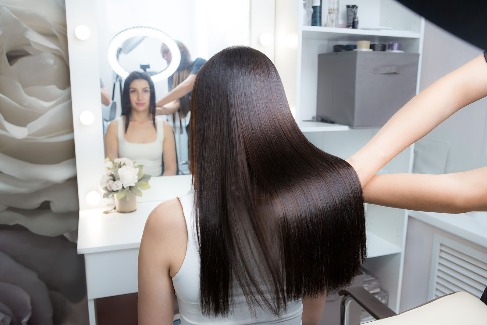 Woman with long, shiny, straight hair looking in the mirror after receiving a keratin hair treatment.