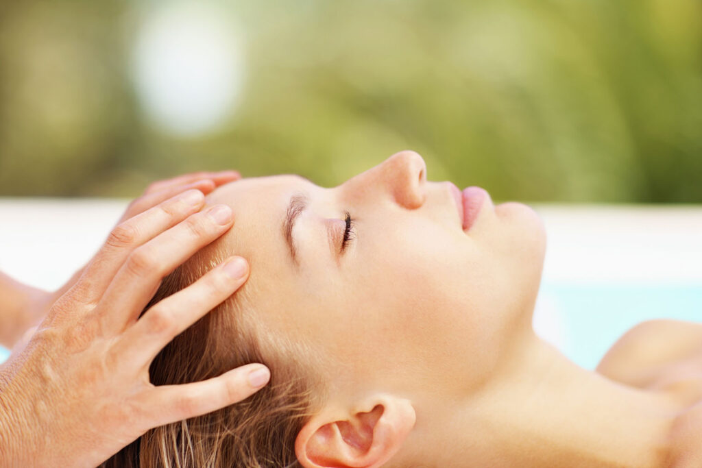 Woman lying peacefully with eyes closed during a calming scalp massage as part of a scalp treatment.
